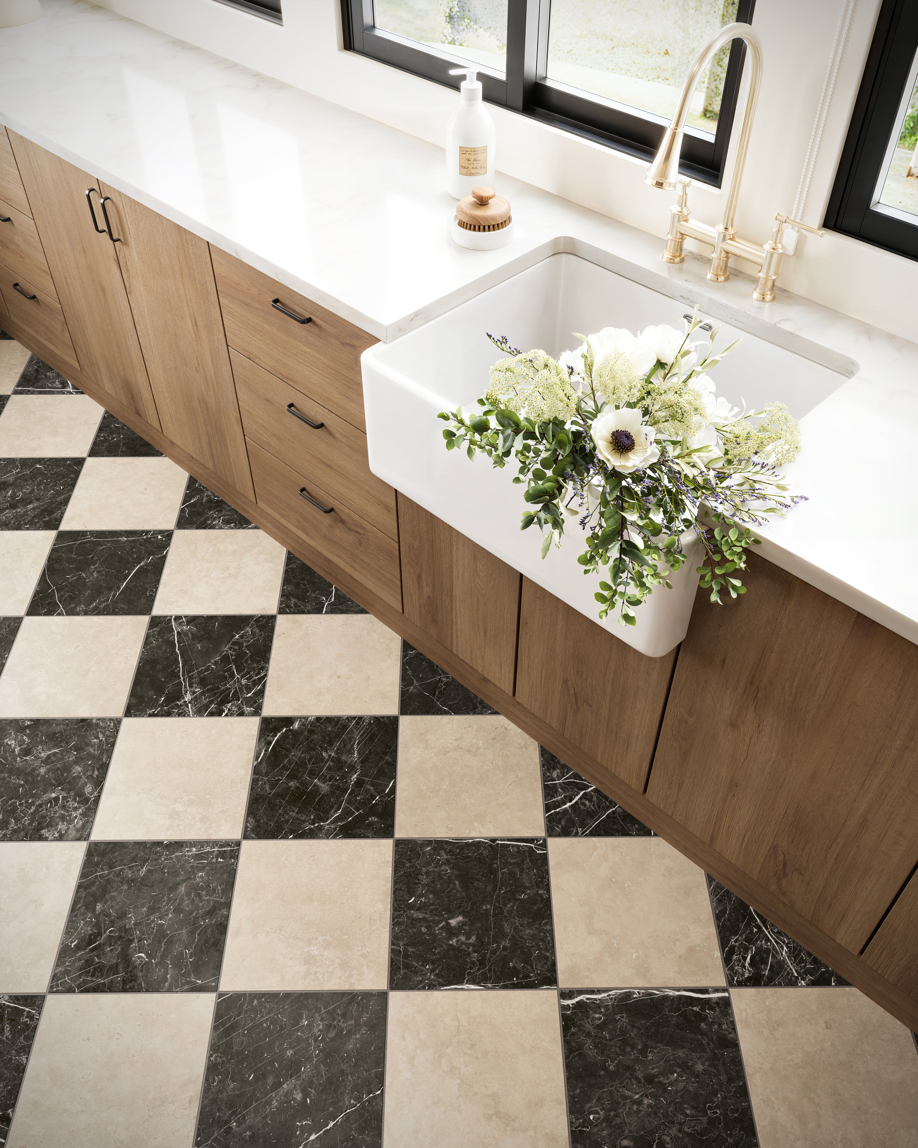 Leona Marfil and Nero Marquina Checkerboard 12x12 Matte tiles complement sleek wooden cabinets and a farmhouse sink adorned with fresh florals.