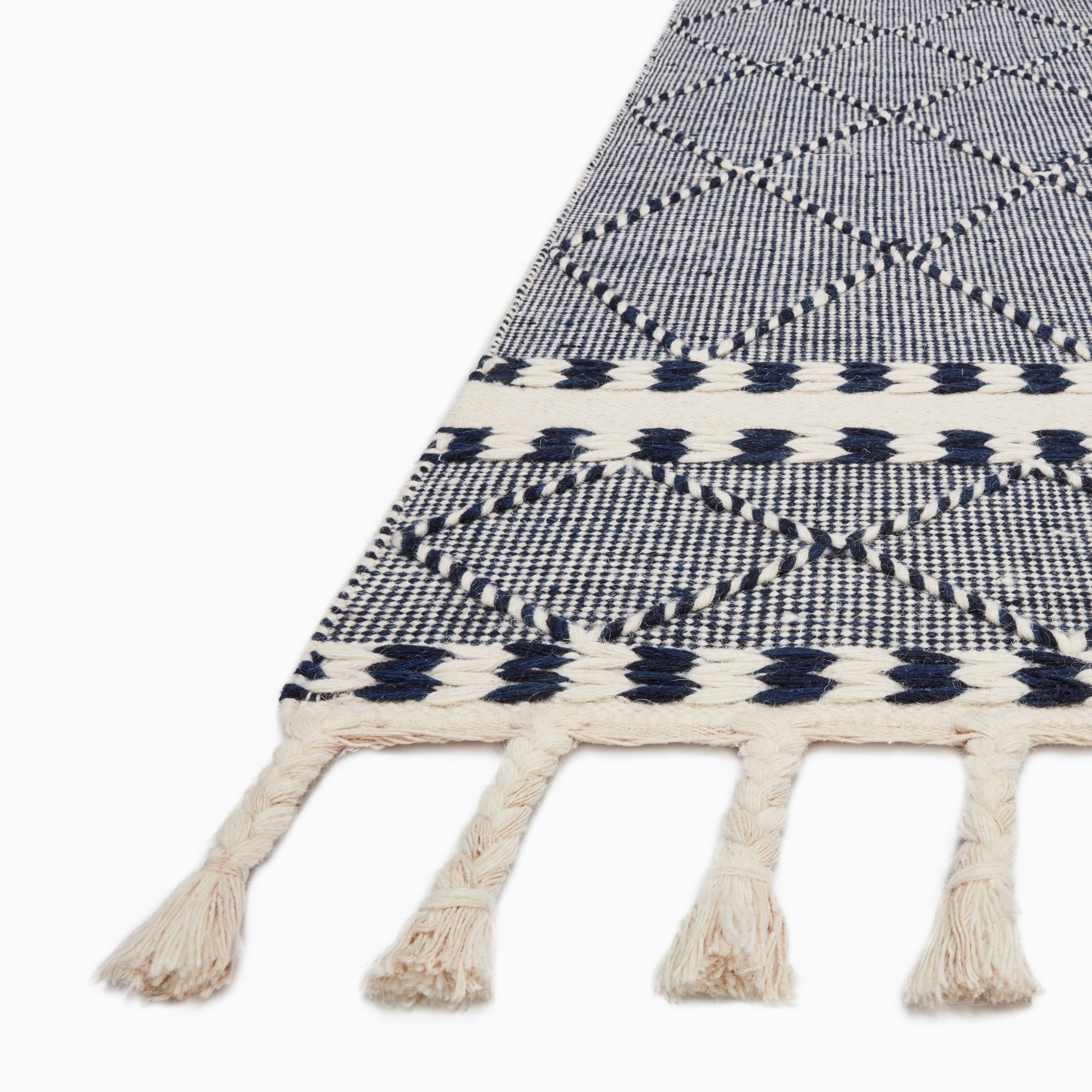 Detailed view of a navy and white rug with a geometric diamond pattern and braided tassel fringe, showcasing its intricate texture.