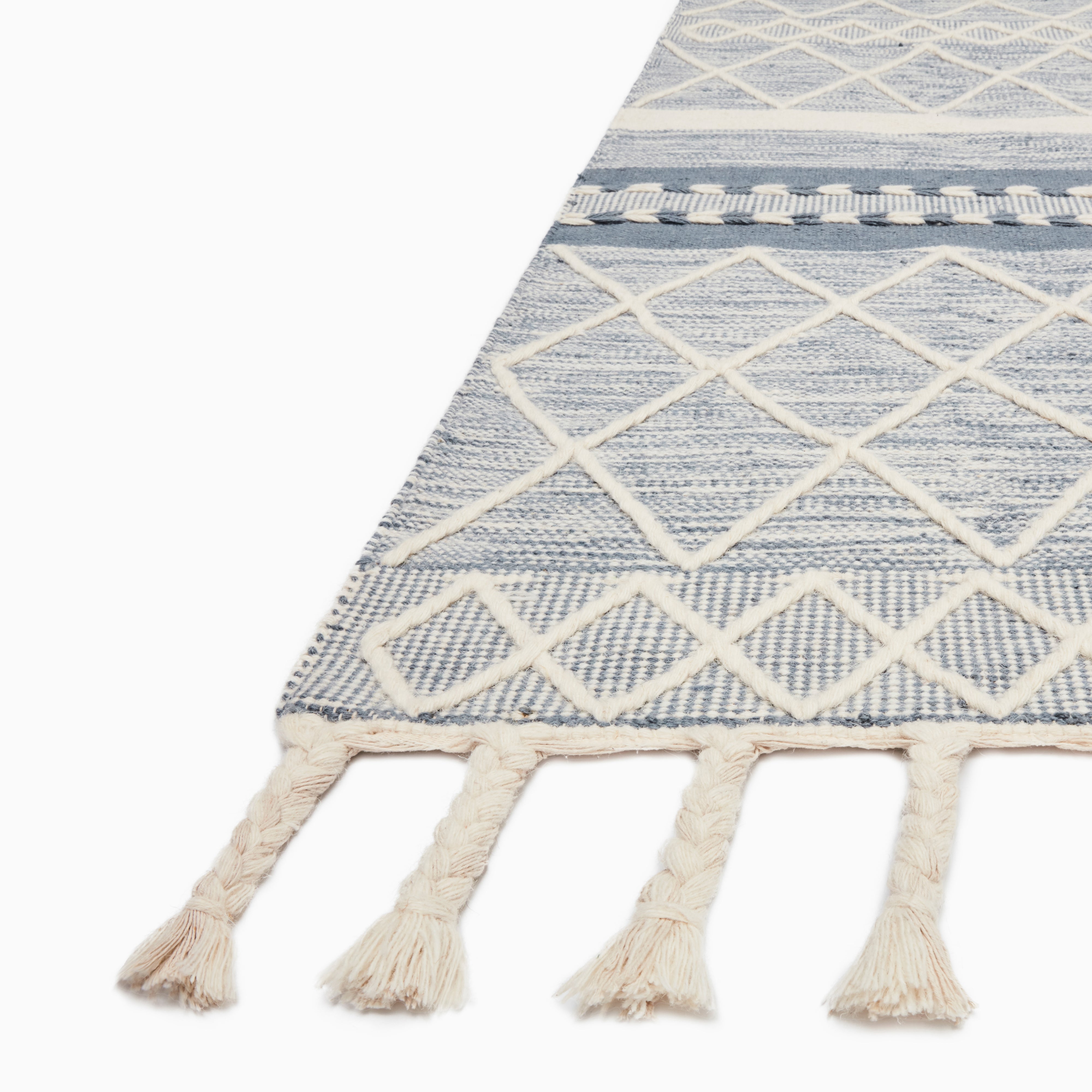 Close-up of a boho-style rug with a blue and white diamond pattern and braided tassels, perfect for adding charm to any space